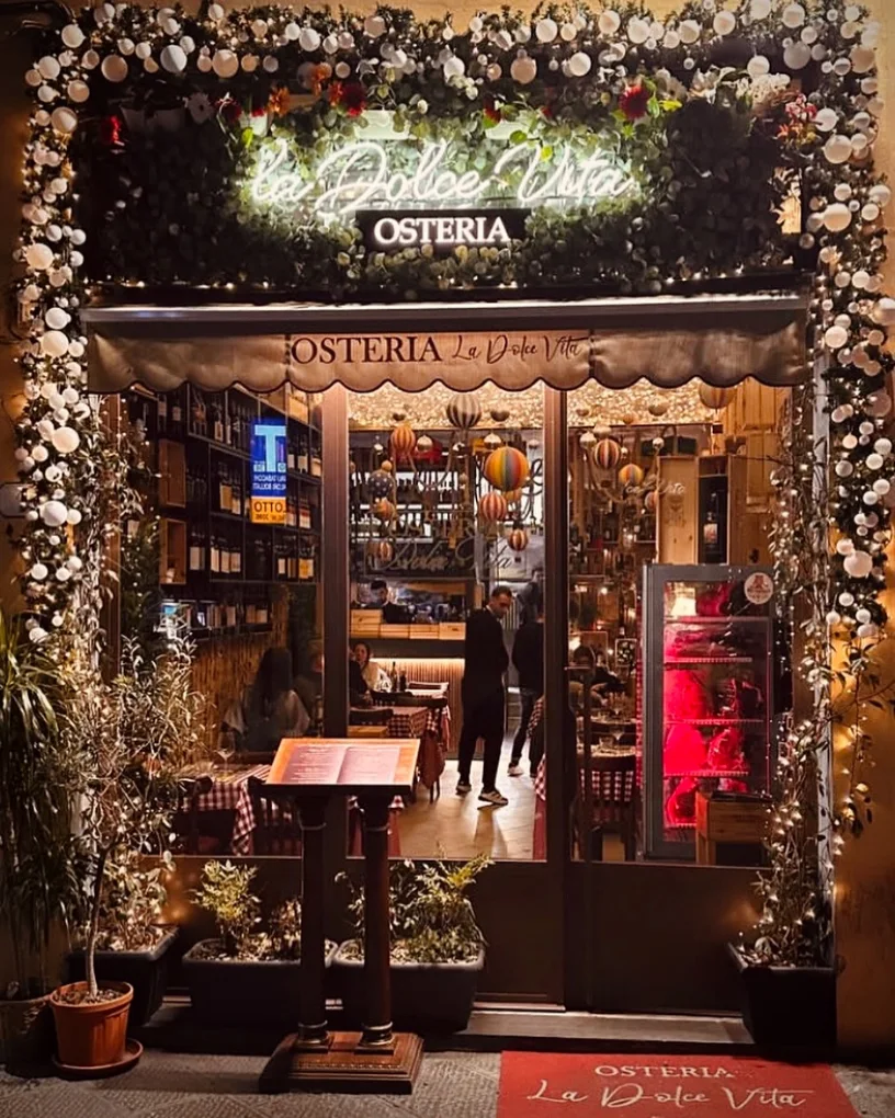 L'ingresso illuminato dell'Osteria La Dolce Vita di sera, con l'insegna al neon e le luci calde