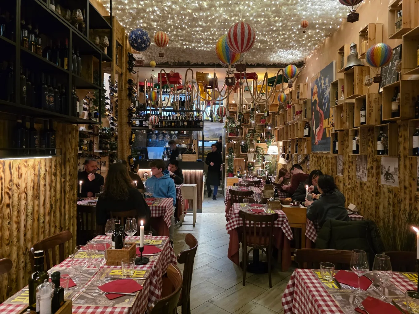 La sala gremita sotto il soffitto di luci calde, candele accese sui tavoli a quadretti